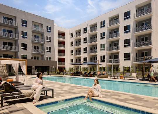 Two women are sitting by a pool in front of apartment buildings.