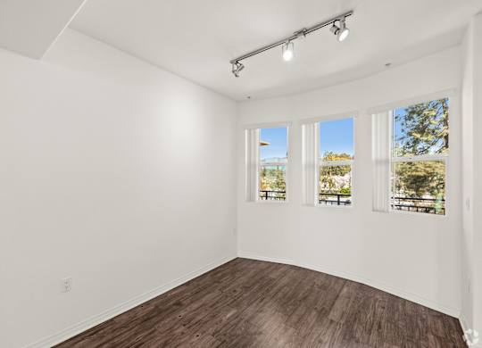 A room with white walls and wooden flooring with three windows.