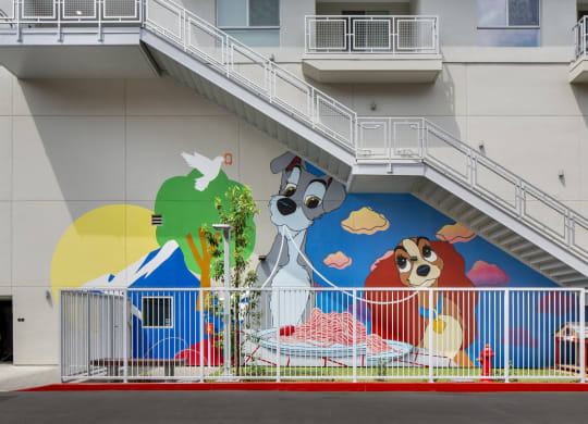 Woodland Hills Lofts for Rent - The Q Variel Apartments - Gated Paw Park with Grass Turf, a Bench, a Red Fire Hydrant, and a Disney Mural