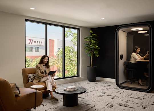 A woman is sitting on a couch in a room with a large window and a plant.
