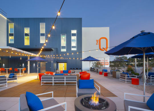 Apartments in Woodland Hills for Rent - The Q Variel Apartments - Patio with String Lights, Plush Outdoor Seating, Umbrellas, Potted Plants, and a Fire Pit