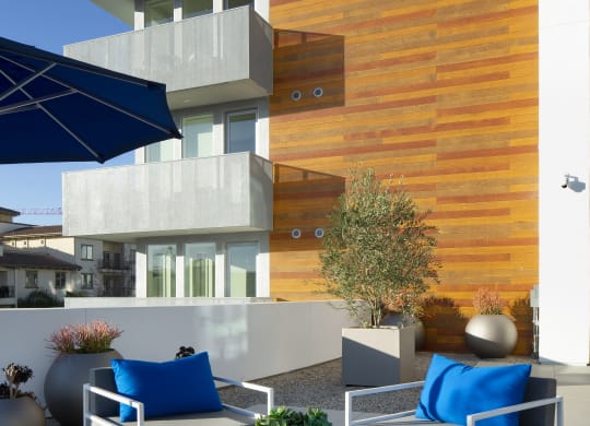 Apartments for Rent in Woodland Hills, CA - The Q Variel Apartments - Outdoor Terrace with High Chairs, Tables, Community Kitchen, Gas BBQ Grills, Potted Plants,  and a Wall-Mounted TV