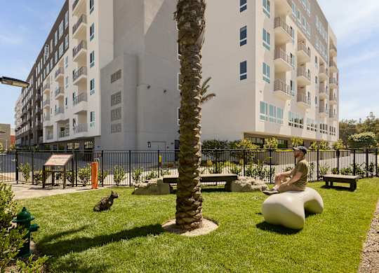 A man is sitting on a white bench in a park with a palm tree and a building in the background.