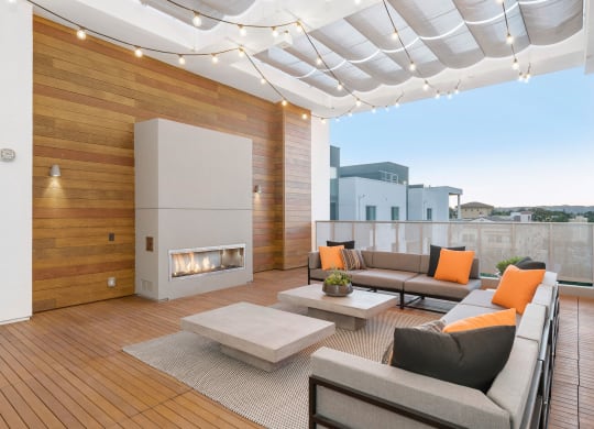 Two Bedroom Apartments in Woodland Hills, CA - The Q Variel - Outdoor Lounge with Couches, a Fireplace, Coffee Tables, String Lights, and City Views