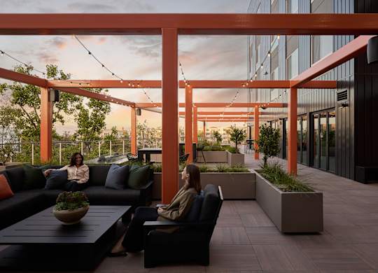 Two women are sitting on a couch under a pergola.