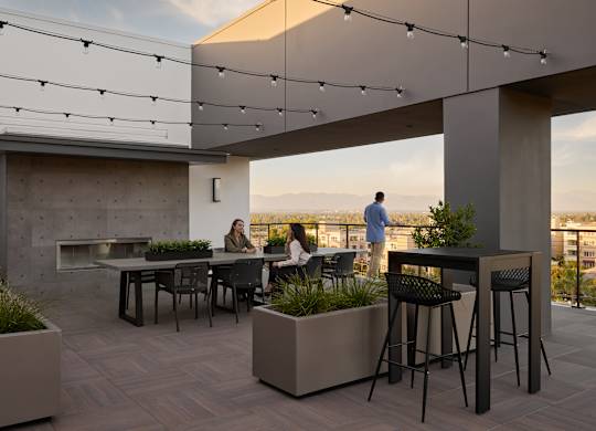 A rooftop patio with people sitting at tables and a view of the city.