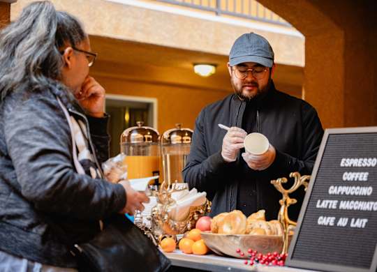 A man in a black outfit is serving coffee to a customer at a cafe.