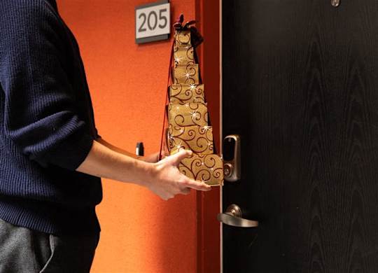 A person holding a bottle of champagne in front of a door with a number 205 on it.