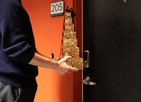 A person holding a bottle of champagne in front of a door with a number 205 on it.