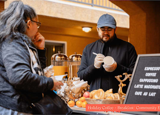 A man in a black outfit is serving coffee to a customer at a holiday coffee breakfast community event.