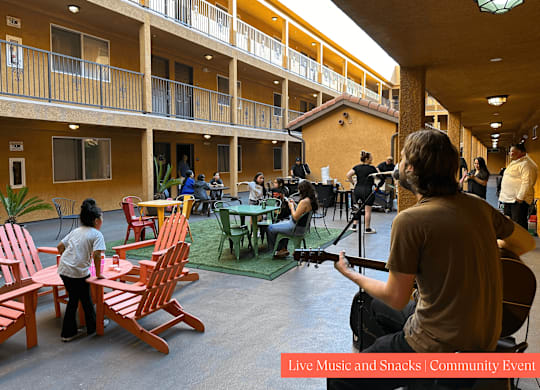 A man is playing a guitar at a live music and snacks community event.