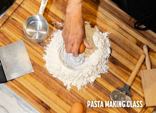 A person is making pasta with a metal scoop and a wooden spatula on a wooden board.