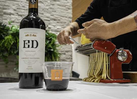 A bottle of Ed Emundo 2013 Cabernet Sauvignon is on a table next to a cup of wine and a pasta maker.
