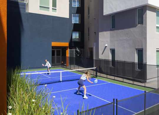 two women playing tennis on a blue court in front of a building