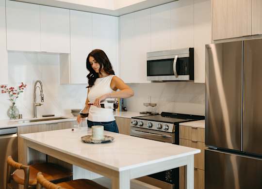 A woman is standing in a kitchen with a white table and a stainless steel refrigerator.