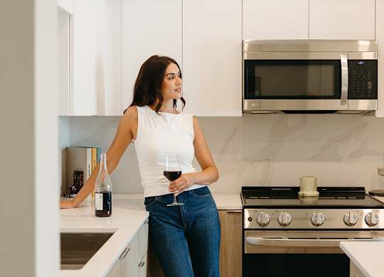 A woman in a white top and blue jeans is standing in a kitchen.