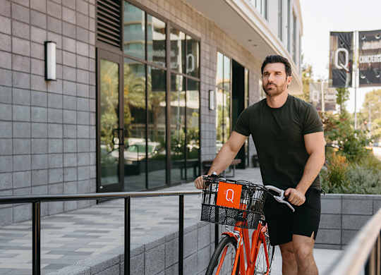 A man is riding a bicycle with a basket on the sidewalk.