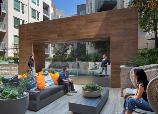 people sitting on couches and chairs on a patio with a wooden wall in the background