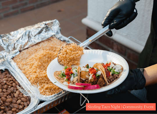 A person is serving food from a plate at a Sizzling Taco Night community event.