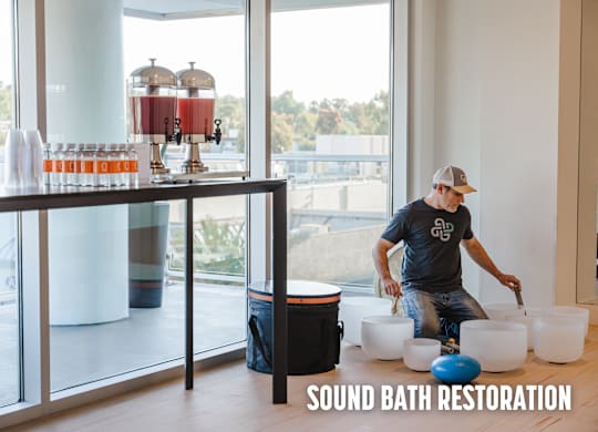 A man is working on a sound bath restoration setup in a room with large windows.