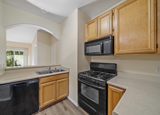 a kitchen with wooden cabinets and black appliances at The Village Apartments, Van Nuys, 91406