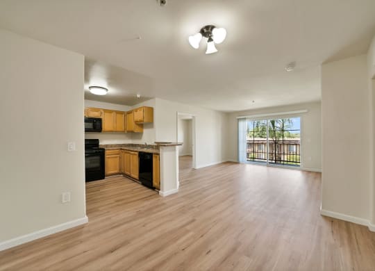 an empty living room and kitchen with wood flooring and a large window