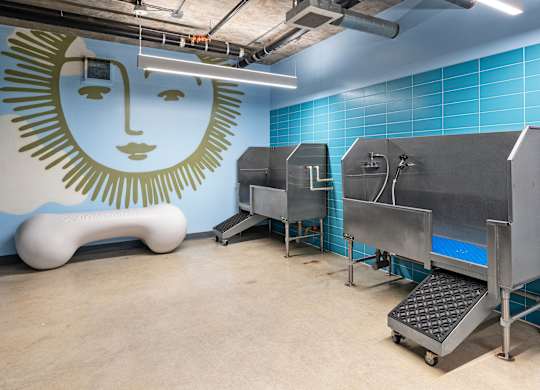 A large industrial machine sits in a room with a blue tiled wall and a mural of a face.