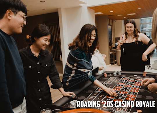 A group of people playing a game on a table with the words "ROARING '20s CASINO ROYALE" on it.