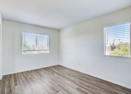 an empty room with wood flooring and two windows