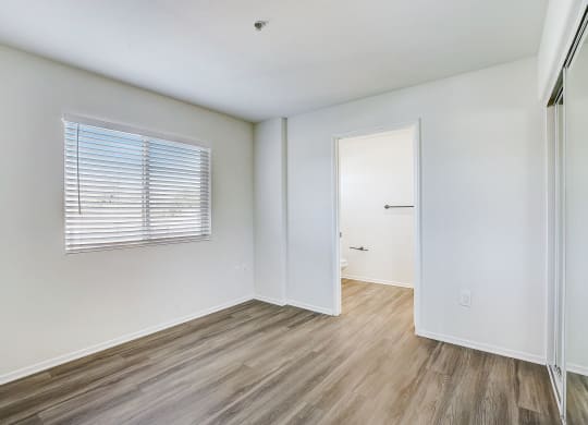 a bedroom with white walls and wood flooring and a door to a closet
