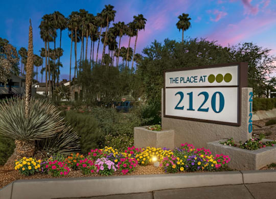 A sign that says "The Place at 2120" is in front of some plants and trees.