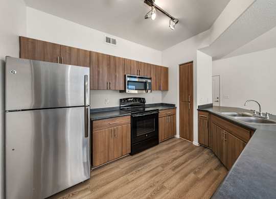 A kitchen with a stainless steel refrigerator, wooden cabinets, and a black countertop.
