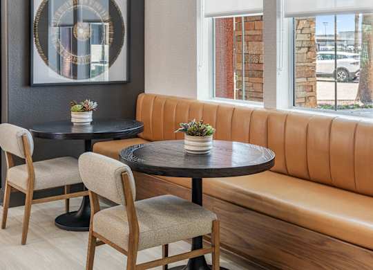 A round table with a plant on it sits in front of a tan booth.