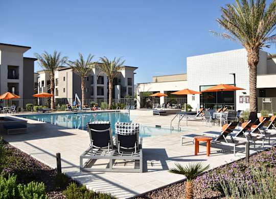 A pool area with chairs and umbrellas in front of a building.