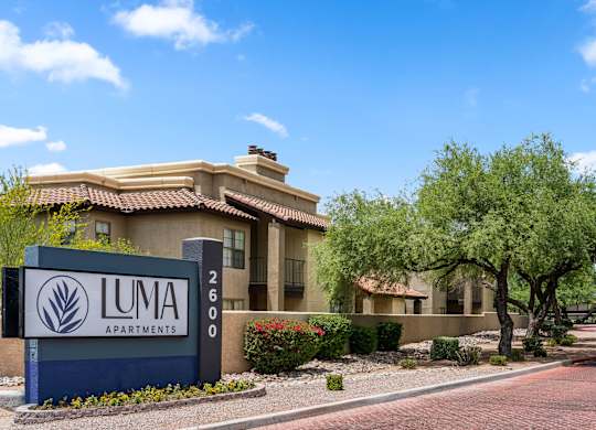 A sign for Luma Apartments is in front of a building with a red roof.