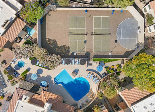 An aerial view of a tennis court and a swimming pool surrounded by buildings.