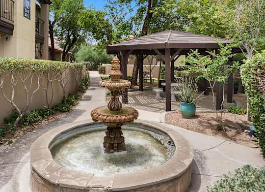 A fountain in the middle of a courtyard with a gazebo in the background.