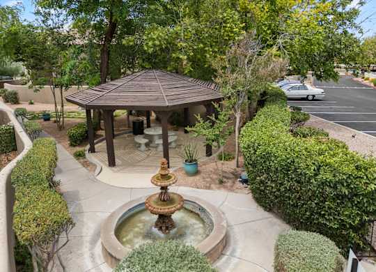 A gazebo with a fountain in the middle of a landscaped area.
