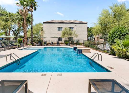 A swimming pool surrounded by palm trees and a building in the background.