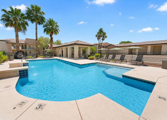 A large swimming pool surrounded by palm trees and a building.