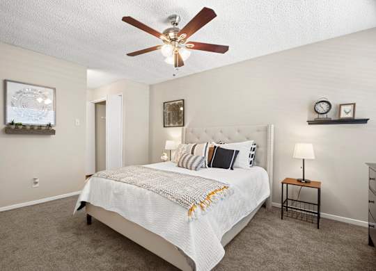 A bedroom with a bed, a ceiling fan, and a nightstand with a lamp.