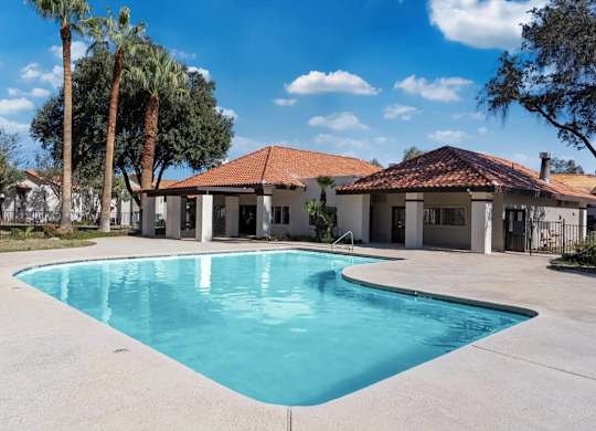 A swimming pool in front of a house with a red tile roof.