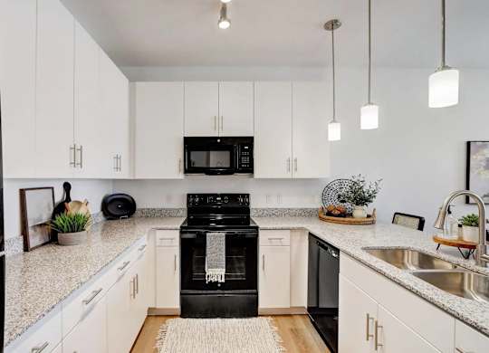 A black refrigerator is in a kitchen with white cabinets.
