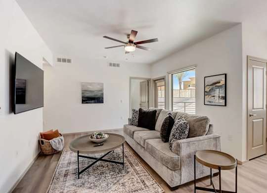 A living room with a grey couch, a coffee table, and a flat screen TV mounted on the wall.