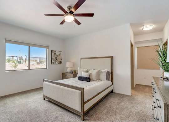 A bedroom with a bed, a ceiling fan, and a window overlooking a patio.