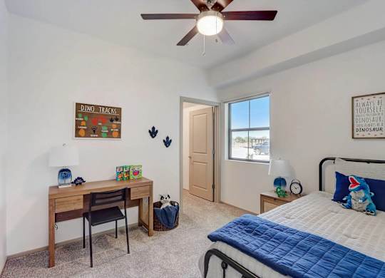A bedroom with a bed, desk, and a ceiling fan.