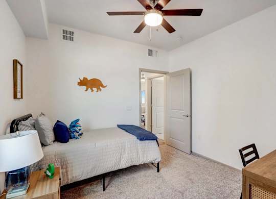A bedroom with a bed, a ceiling fan, and a wooden table.