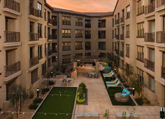A sunset view of a courtyard with a green lawn and apartment buildings.