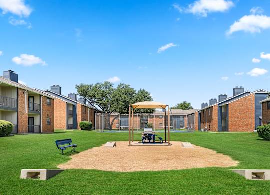 A playground with a swing set and a sandbox in the middle of a grassy area.
