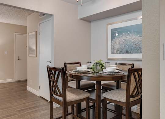 A dining room with a table set for two and a painting on the wall.